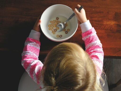 girl eating cereal in white ceramic bowl on table